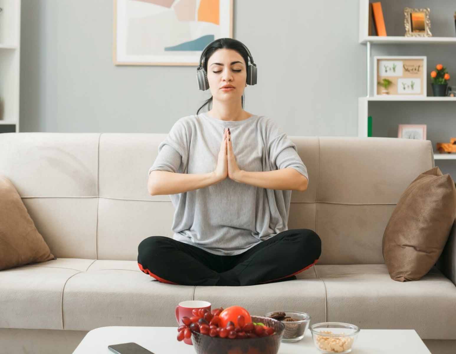 Woman meditating on couch, wearing headphones